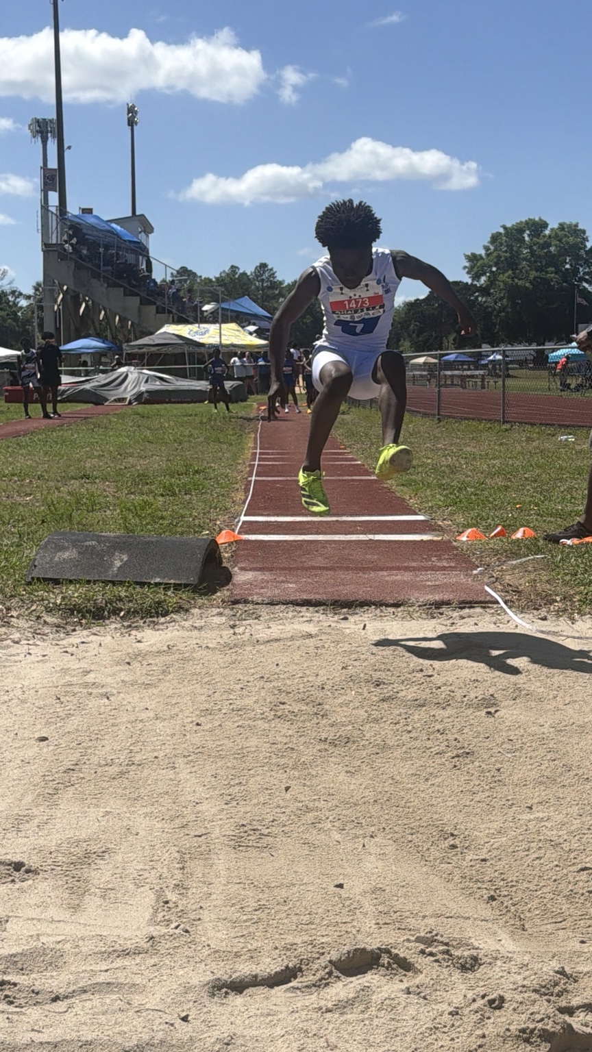 Young track athlete in white uniform airborne on the long jump runway