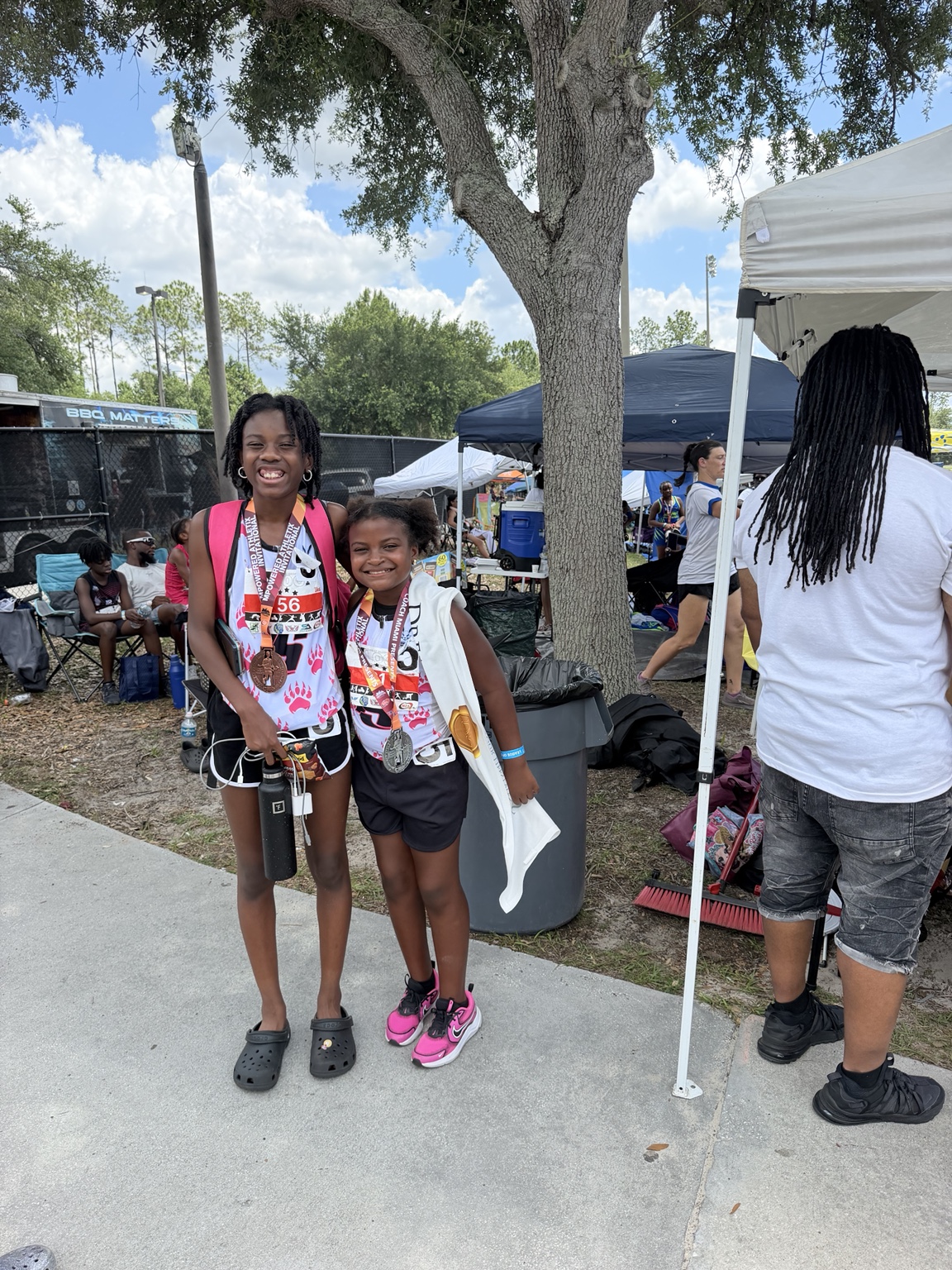 Two young athletes smiling together at a meet with medals