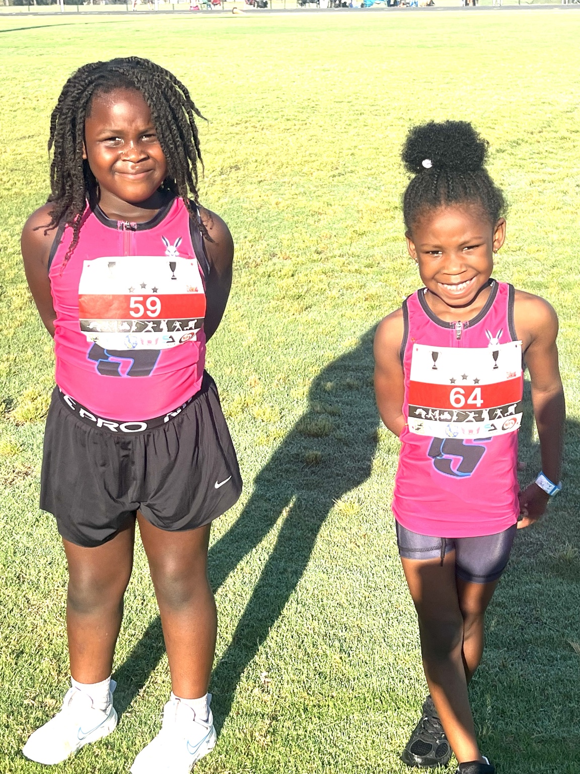Two young athletes in pink uniforms standing together on the grass